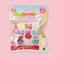 A Calico Critters collectible bunny costume toy in its original retail packaging, featuring five different colored bunny outfits on the front of the bag, set against a solid pastel pink background.
