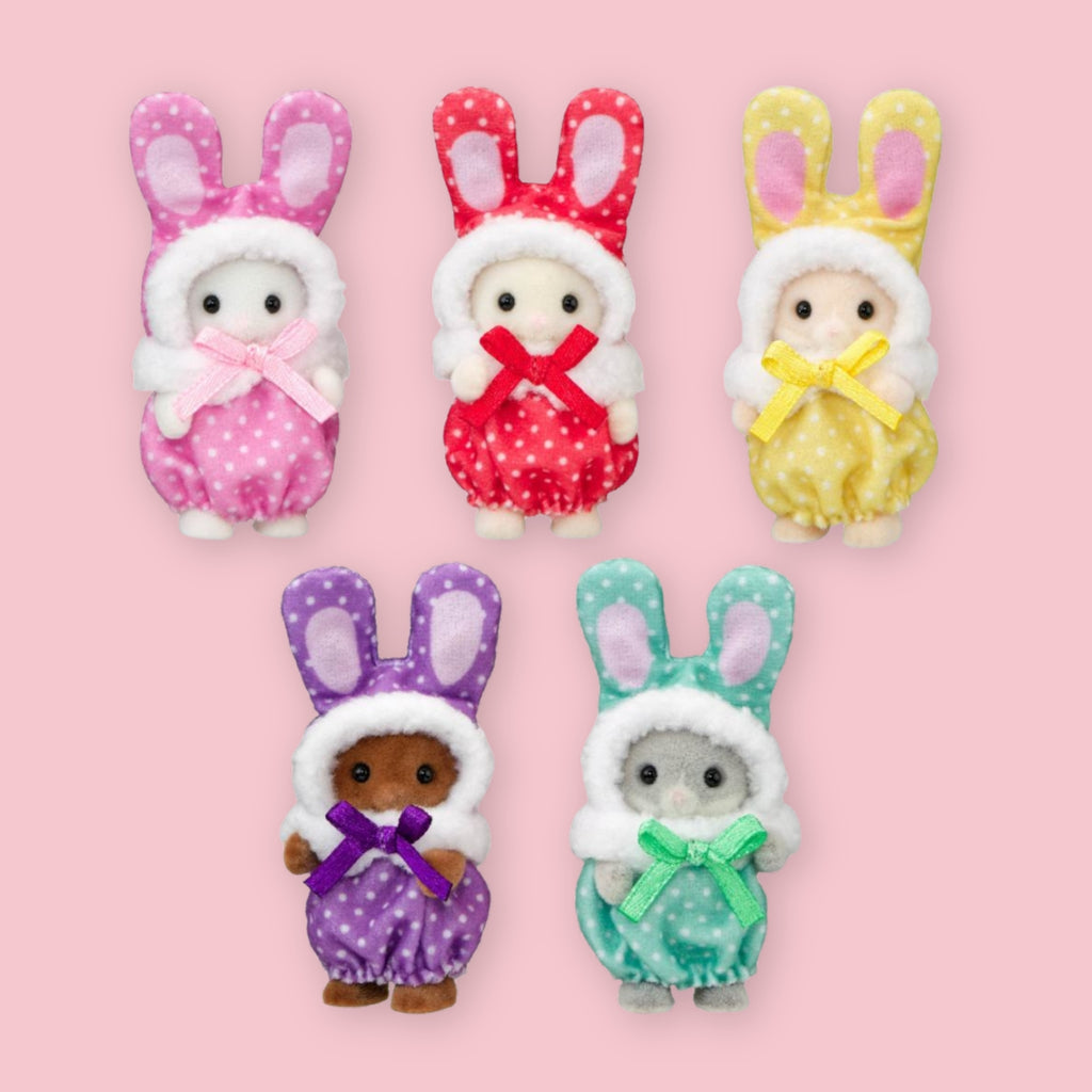 Five small Calico Critters bunny figures wearing colorful polka-dot hooded outfits are arranged on a light pink background. The outfits are pink, red, yellow, purple, and mint green, with white faux-fur trim and matching bows.