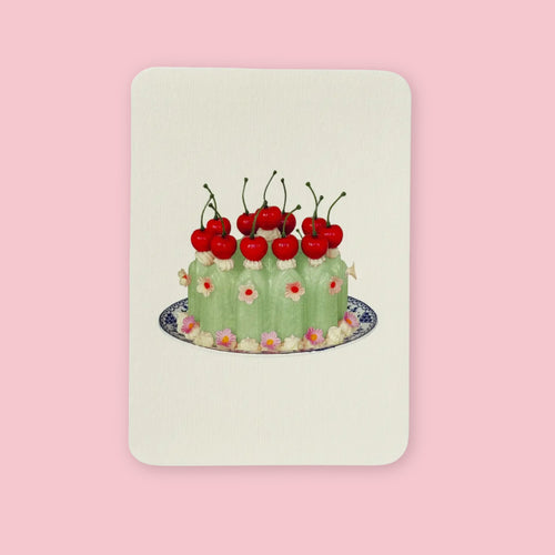 Canonbury Press greeting card featuring an illustrated green chartreuse cake topped with bright red cherries and small floral decorations, centered on a soft cream background.