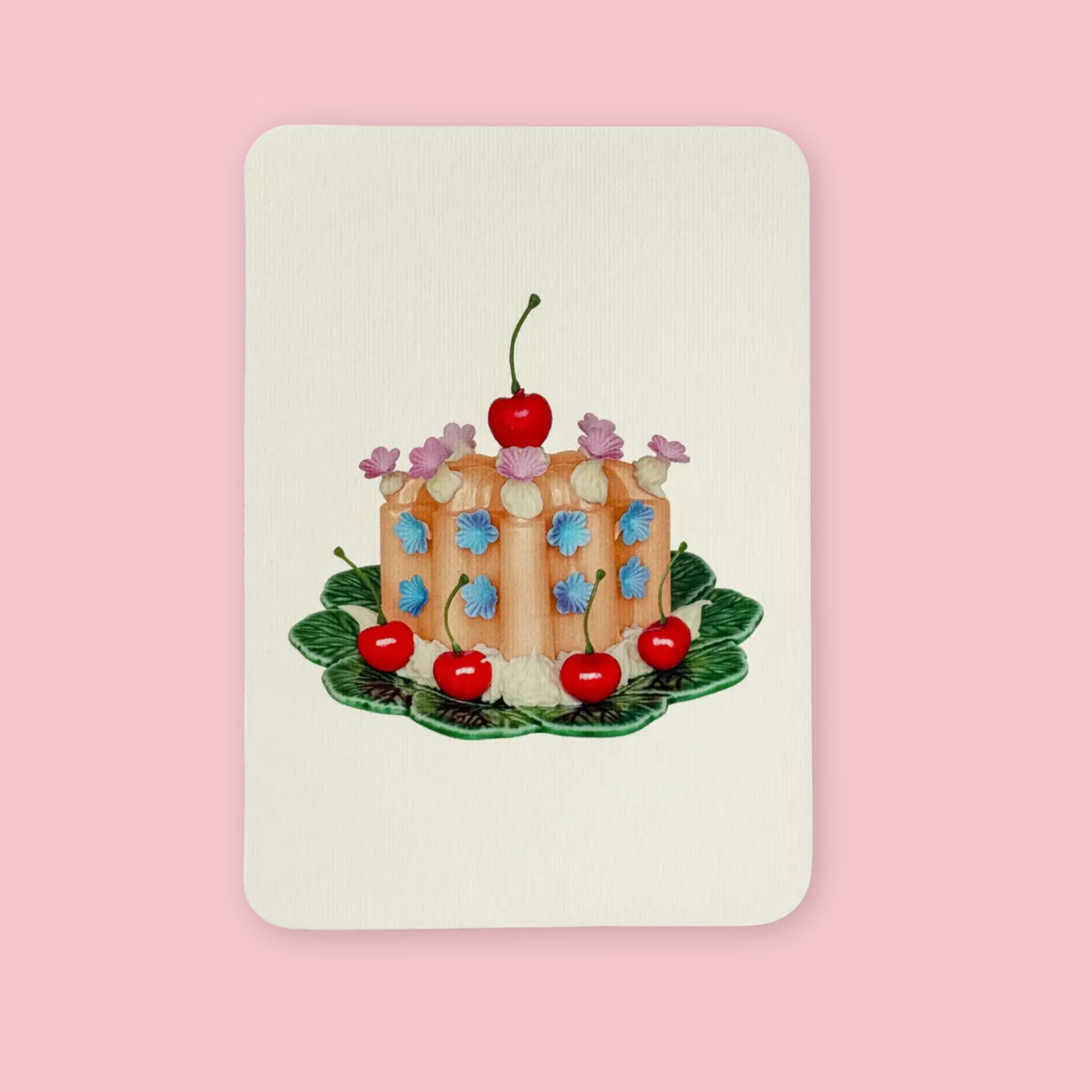 Canonbury Press greeting card featuring an illustrated orange cake with blue flowers, white icing, cherries, and a large cherry on top, displayed on a green leaf plate.