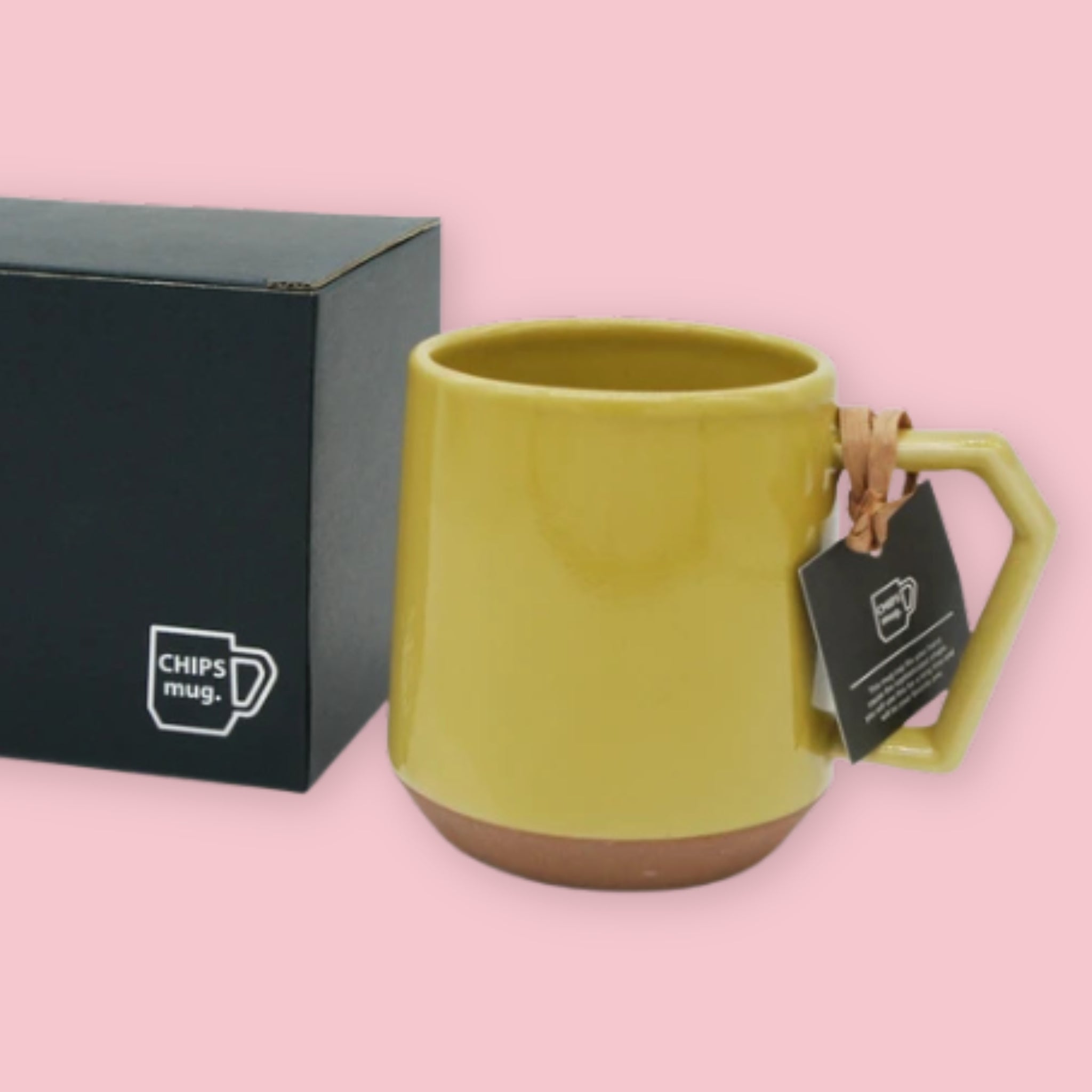 Chips Mug in Mustard with matte yellow glaze and terracotta base with branded black gift box on a pink background.