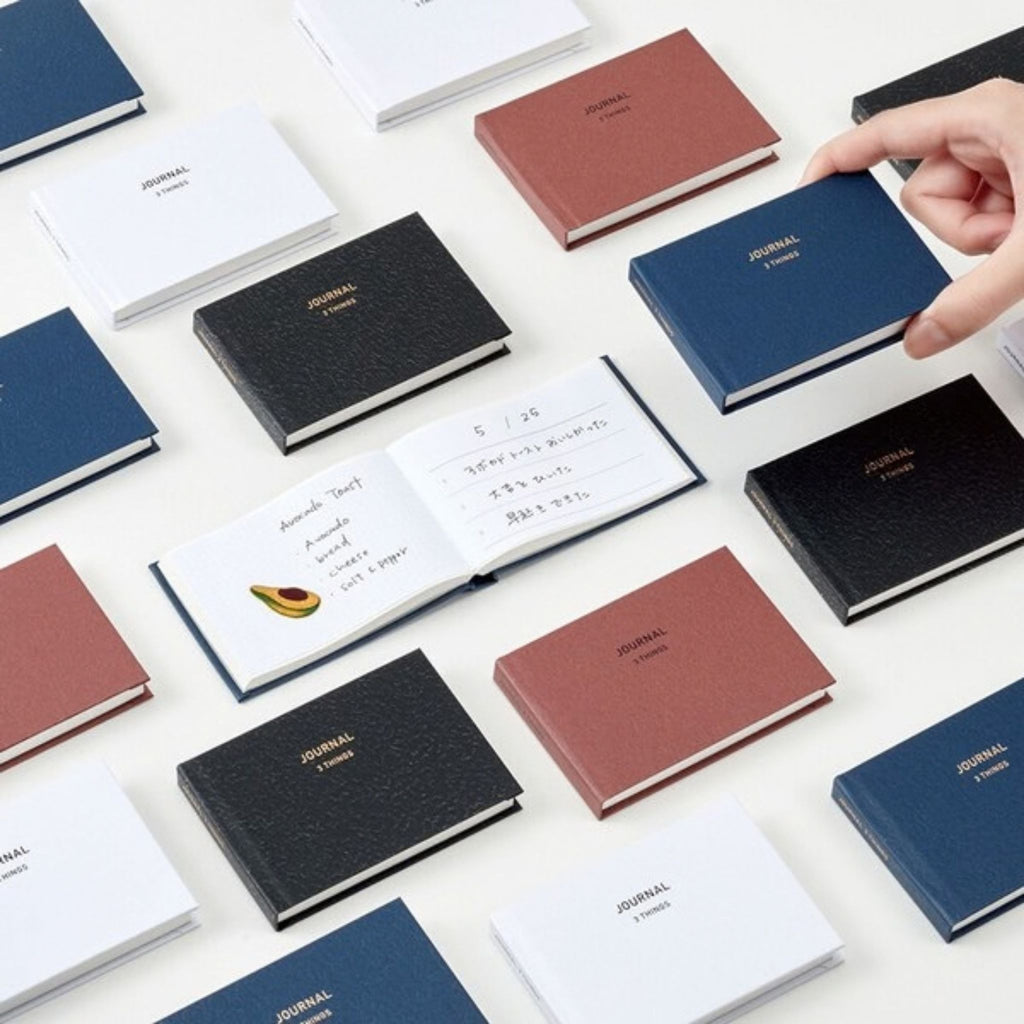 Daigo Mini Easy Journal 3 Things in navy, black, dark red, and white, with an open journal showing daily entries.