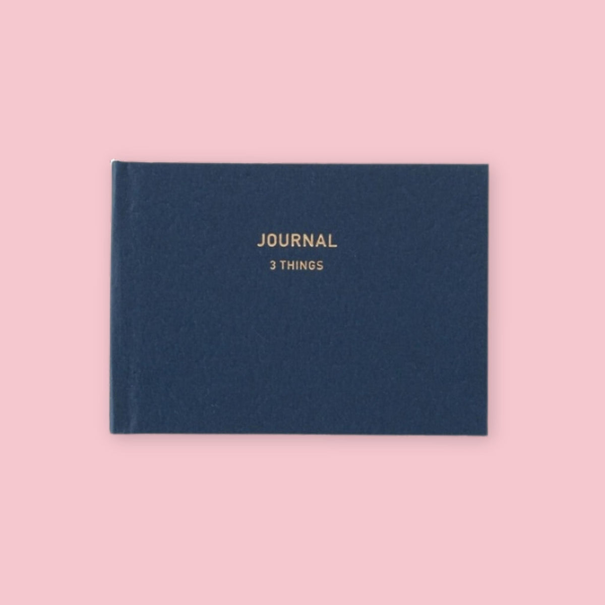 Navy blue Daigo Mini Easy Journal 3 Things with gold lettering on a pink background.
