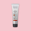 Silver tube of mikan hand cream with a black cap and orange label, shown upright on a pink background.