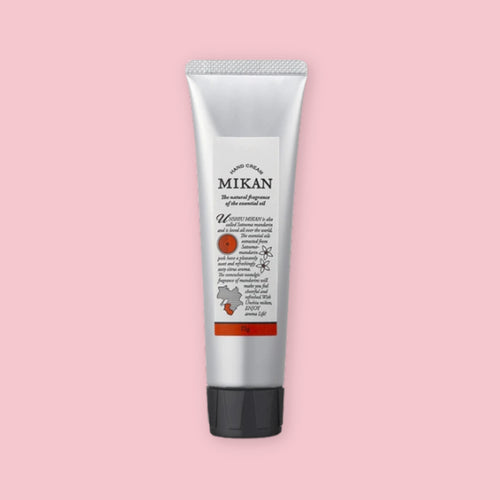 Silver tube of mikan hand cream with a black cap and orange label, shown upright on a pink background.