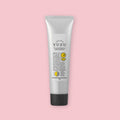 Silver tube of yuzu hand cream with a black cap, shown upright on a pink background.