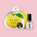 Yuzu nail oil with yuzu-shaped packaging and a small glass bottle with a black cap, shown on a pink background.
