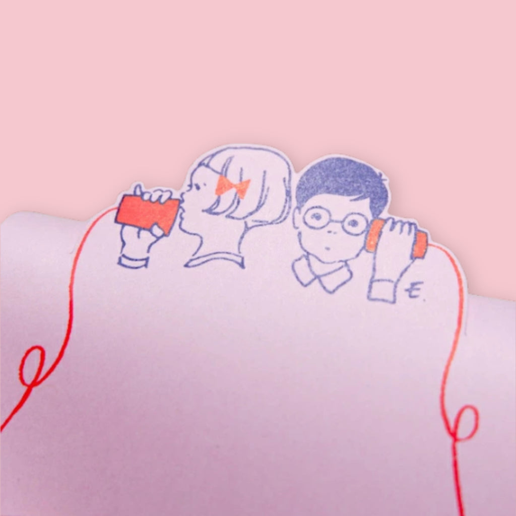 Close-up of illustrated boy and girl connected by a red string on a die-cut memo pad