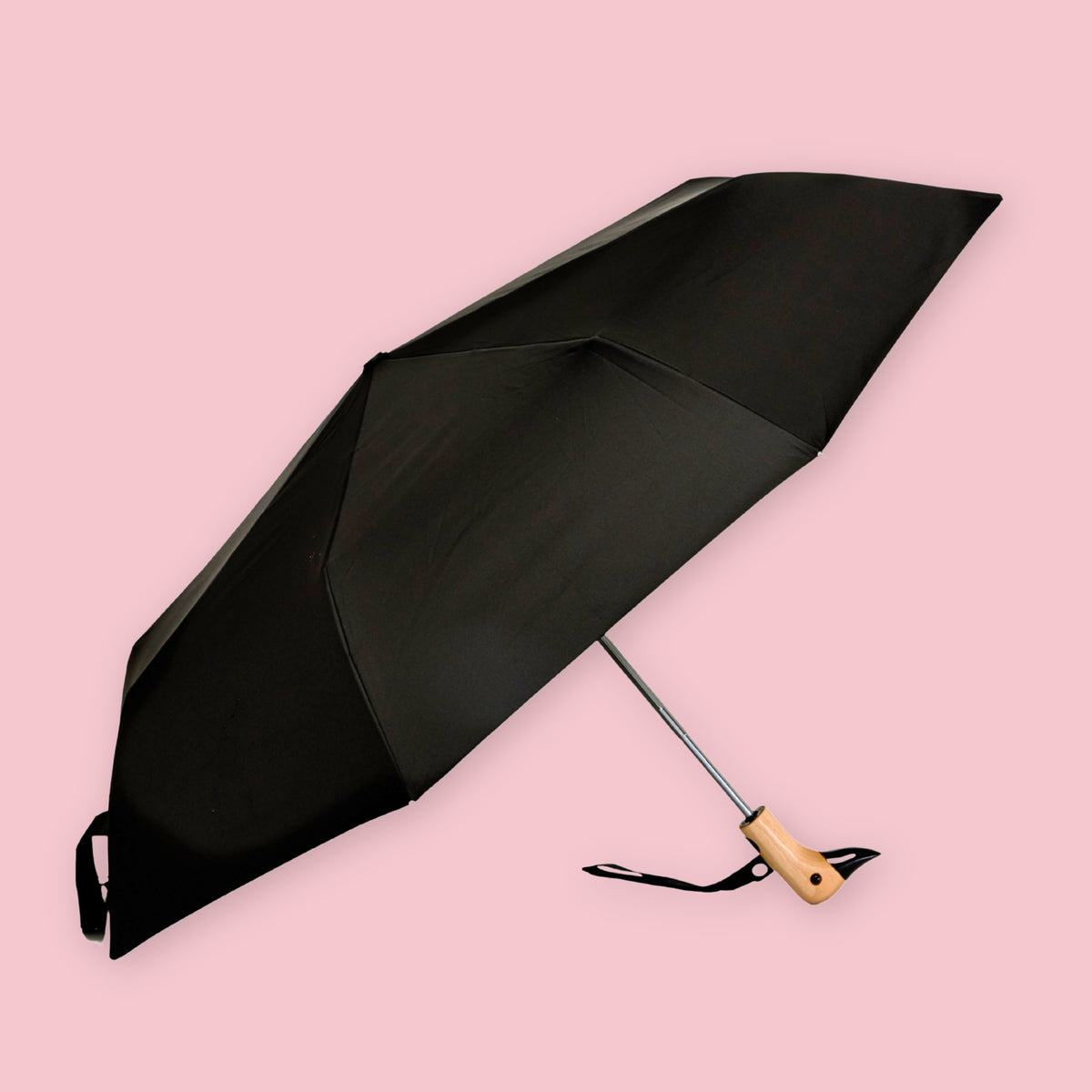 Black folding umbrella with wooden duck-shaped handle open against a pale pink background.