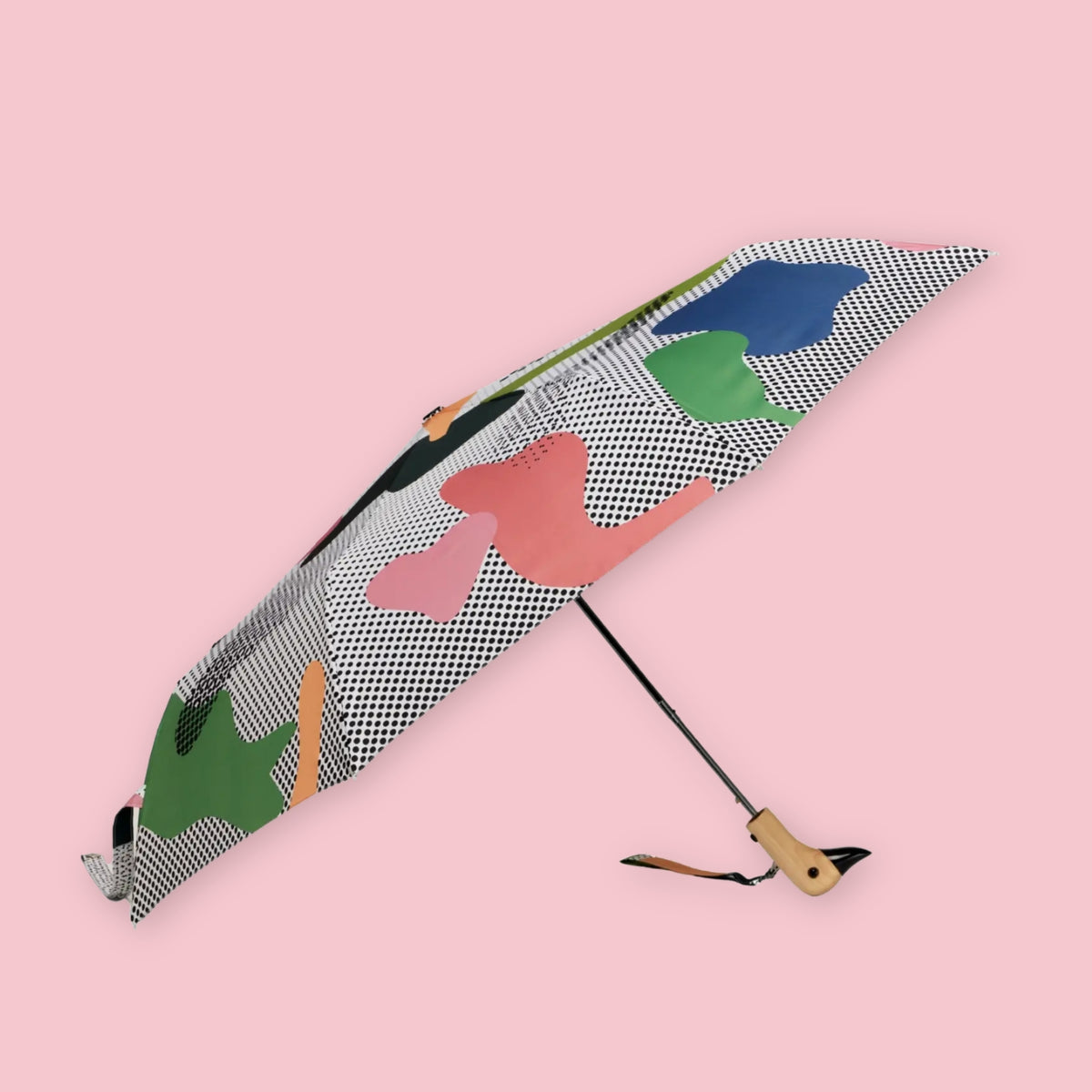 Folding umbrella with abstract dot print and wooden duck-shaped handle open against a pale pink background.