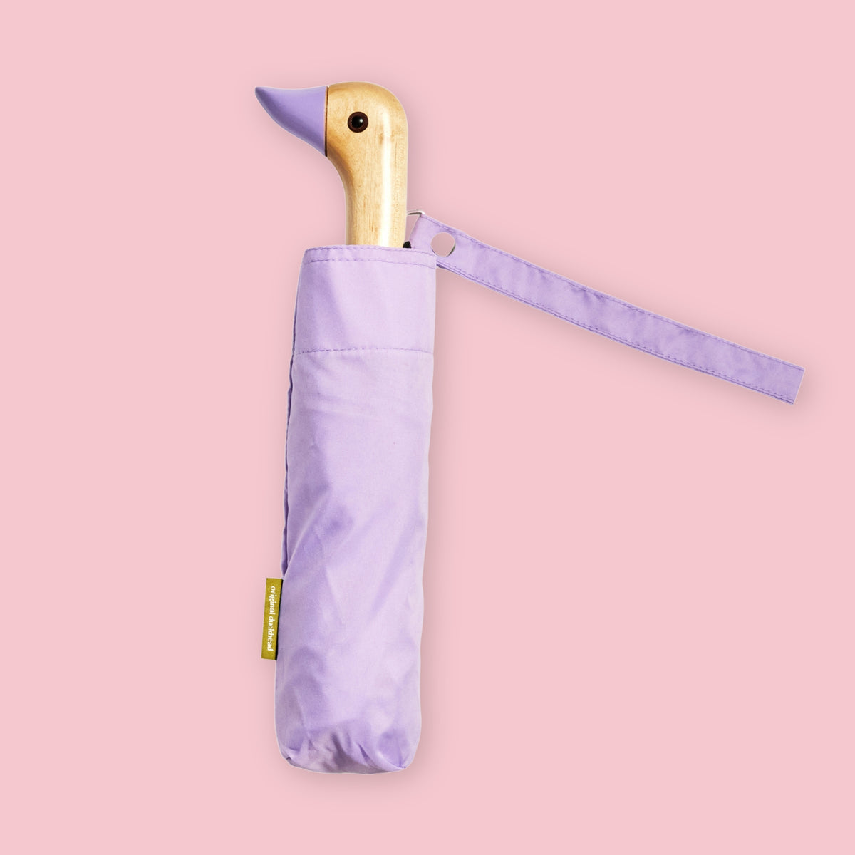 Lilac folding umbrella with duck-shaped wooden handle and matching wrist strap on a pale pink background.