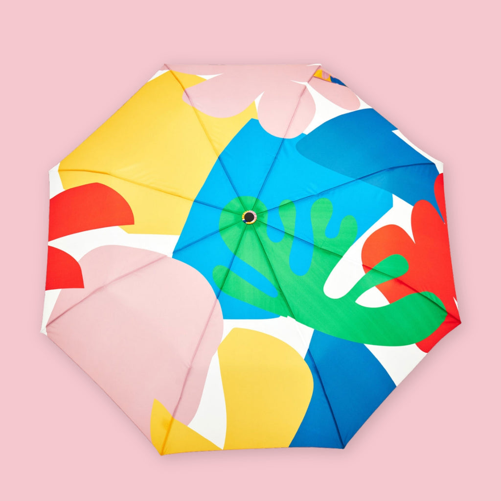 Duckhead compact umbrella with bright abstract print in blue, green, red, yellow, and pink, shown open on a pink background.