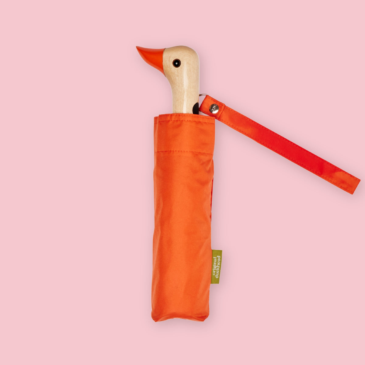 Orange folding umbrella with duck-shaped wooden handle and matching wrist strap on a pale pink background.