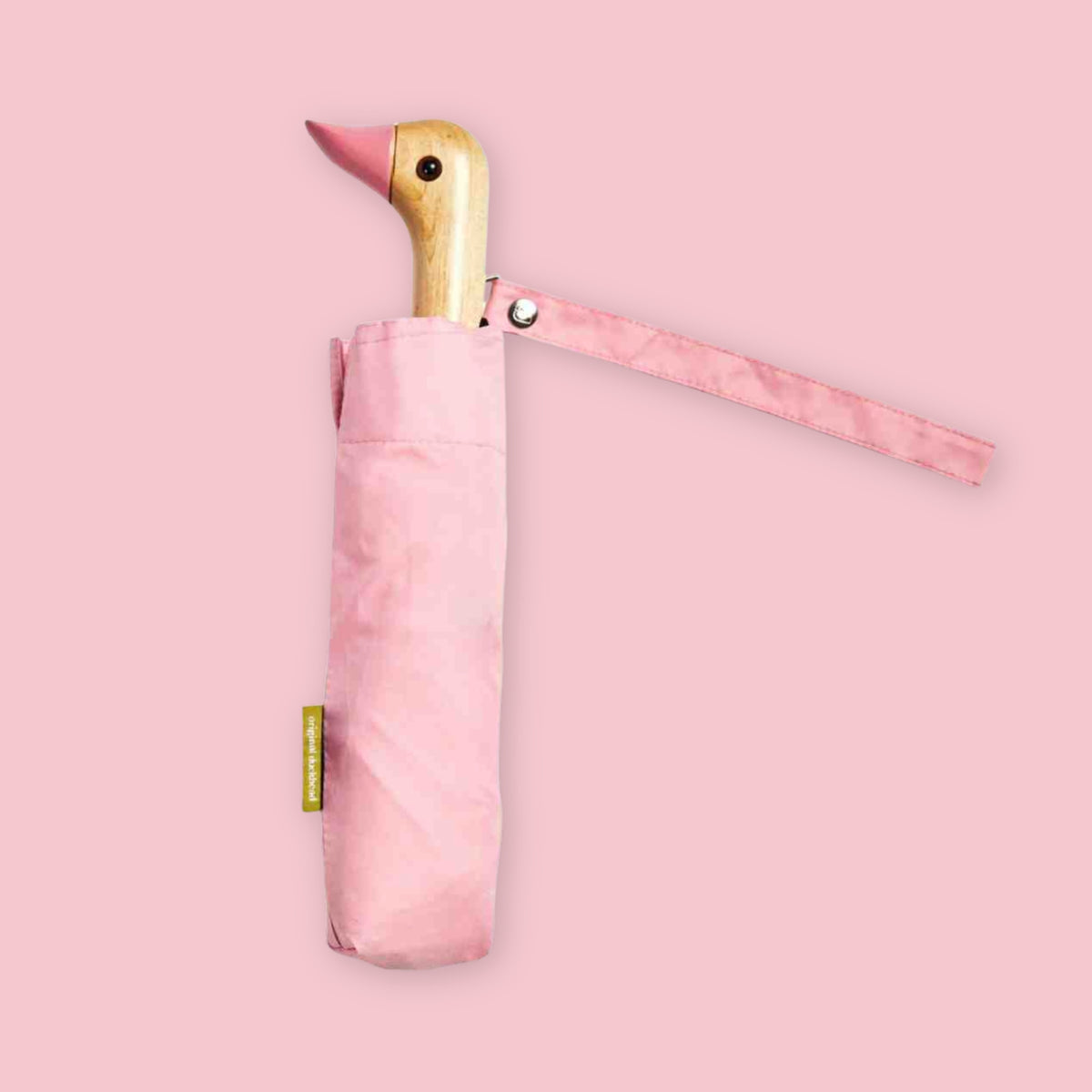 Pink folding umbrella with duck-shaped wooden handle and matching wrist strap on a pale pink background.