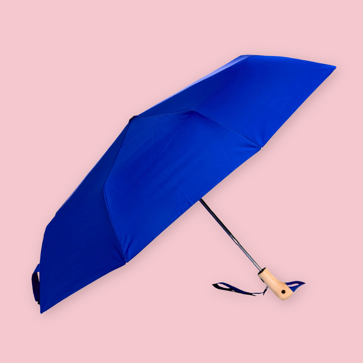 Royal blue folding umbrella with wooden duck-shaped handle open against a pale pink background.