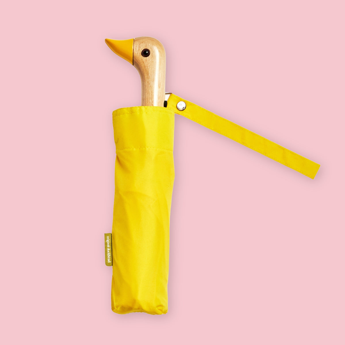 Yellow folding umbrella with duck-shaped wooden handle and matching wrist strap on a pale pink background.