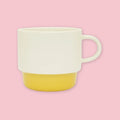 El Commun mug in cream with yellow base on a pink background