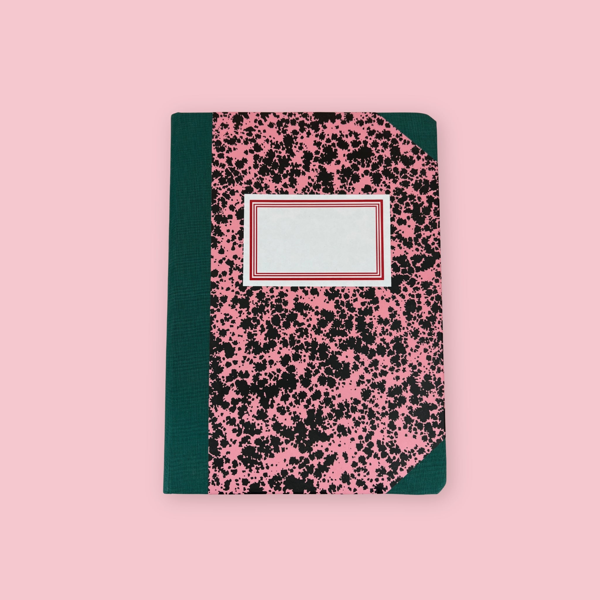 Green and pink patterned notebook with blank label, shown against a pink background.
