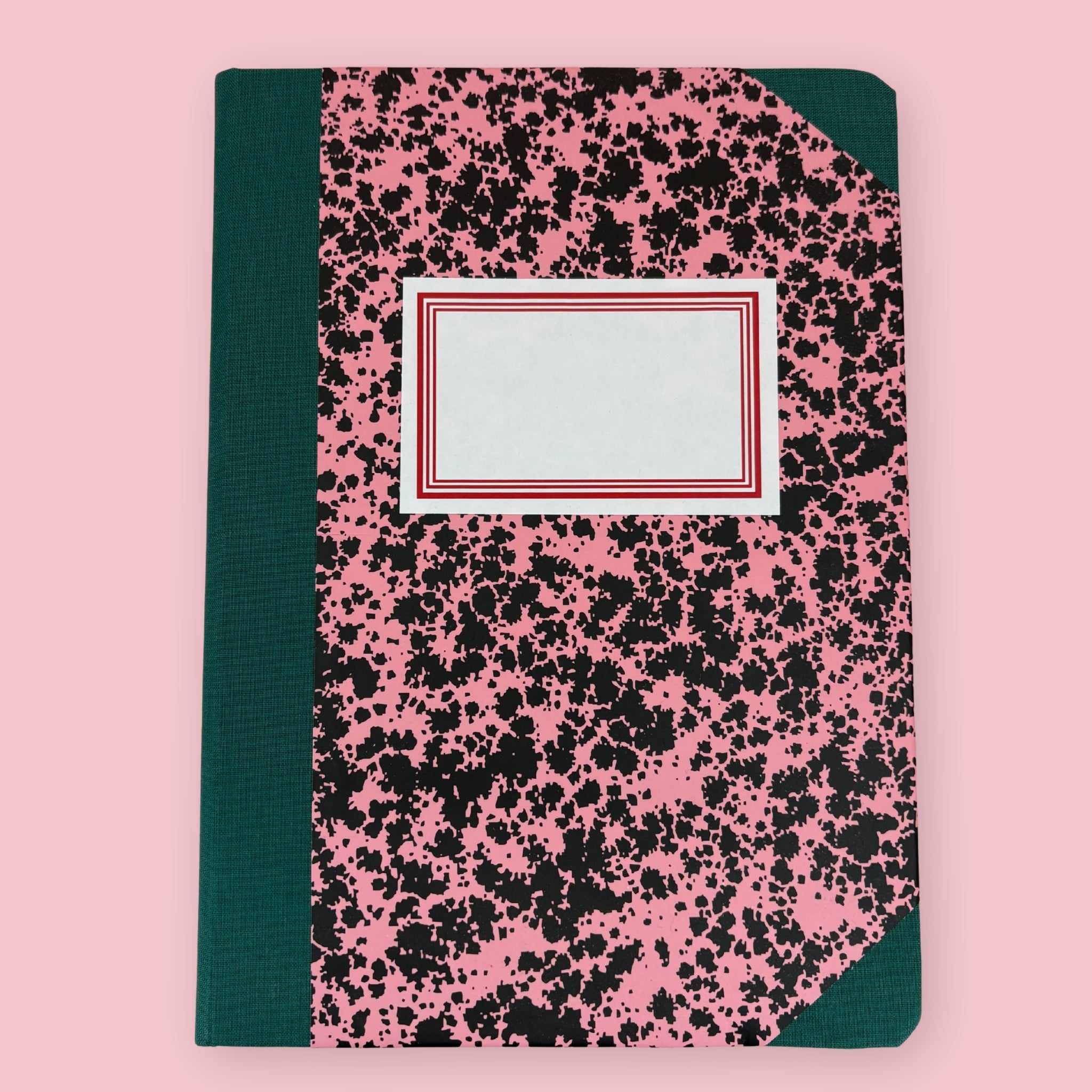 Green and pink patterned notebook with blank label, shown against a pink background.