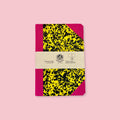 Pink and yellow patterned notebook with paper band, shown against a pink background.