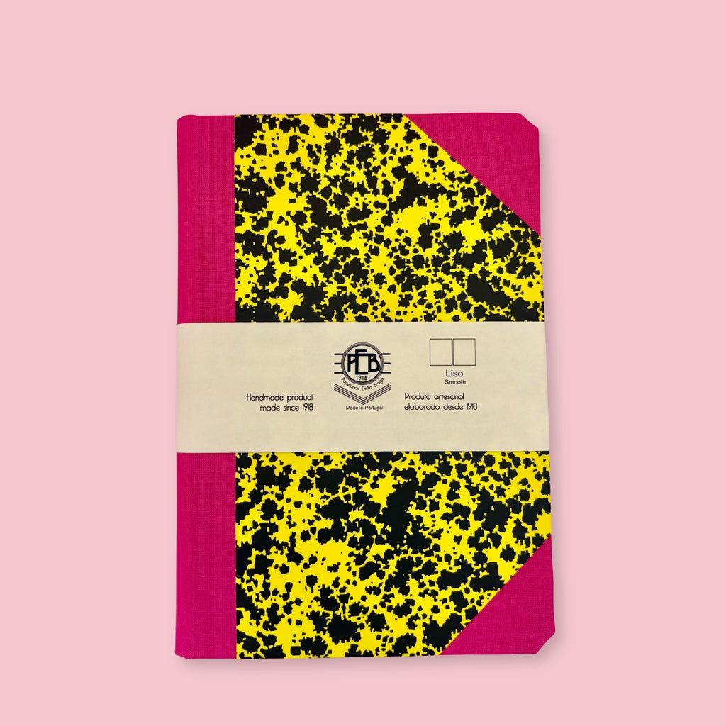 Pink and yellow patterned notebook with paper band, shown against a pink background.