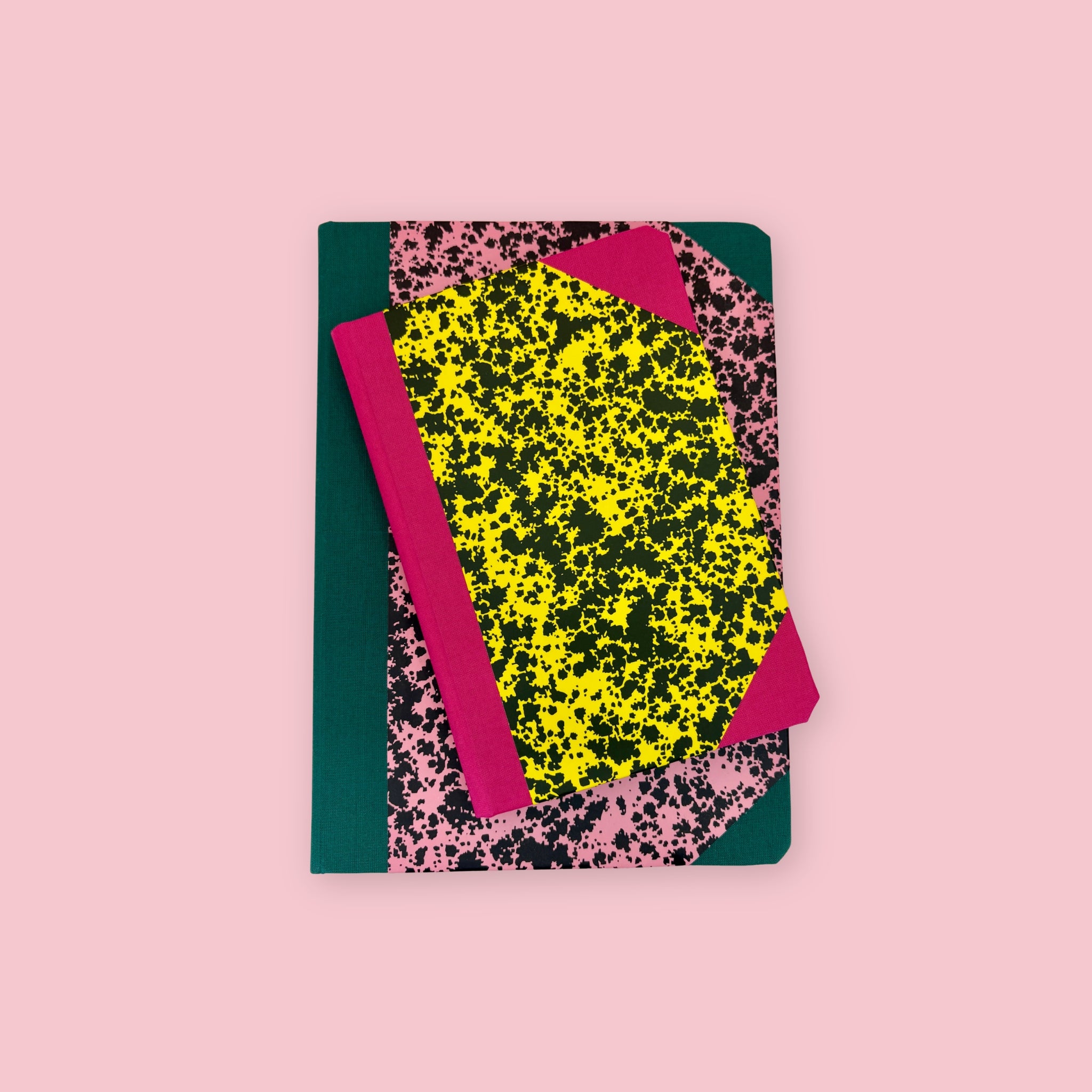 Two patterned notebooks with pink, yellow, black, and green covers, shown stacked against a pink background.