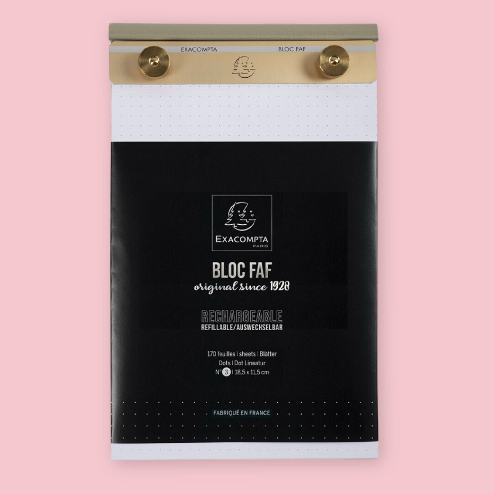 Exacompta Bloc FAF brass desk pad in the 5.25 x 8.25 dot grid size, showing the gold brass bar and knobs holding dot grid paper above the black branded packaging, on a pink background.