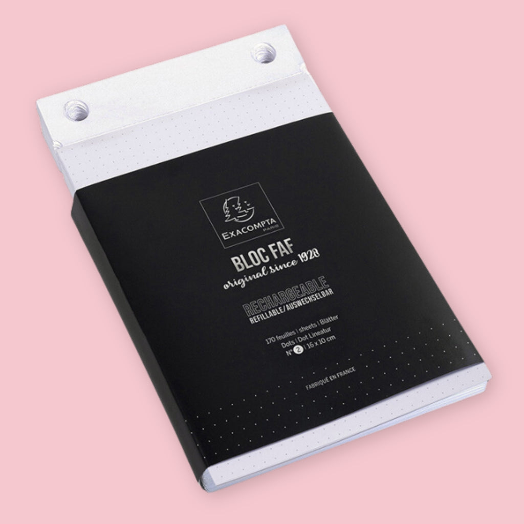 Exacompta Bloc FAF dot grid refill paper for the 5.25 x 8.25 brass desk pad, shown in its black branded packaging with white binding holes visible at top, on a pink background.