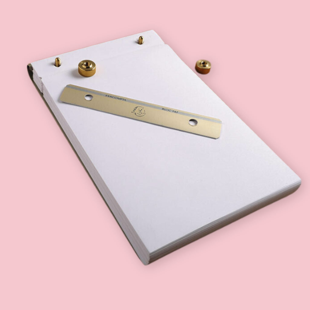Exacompta brass desk pad with blank paper shown disassembled, with the brass bar and knobs removed and resting on top of the paper stack, on a pink background.