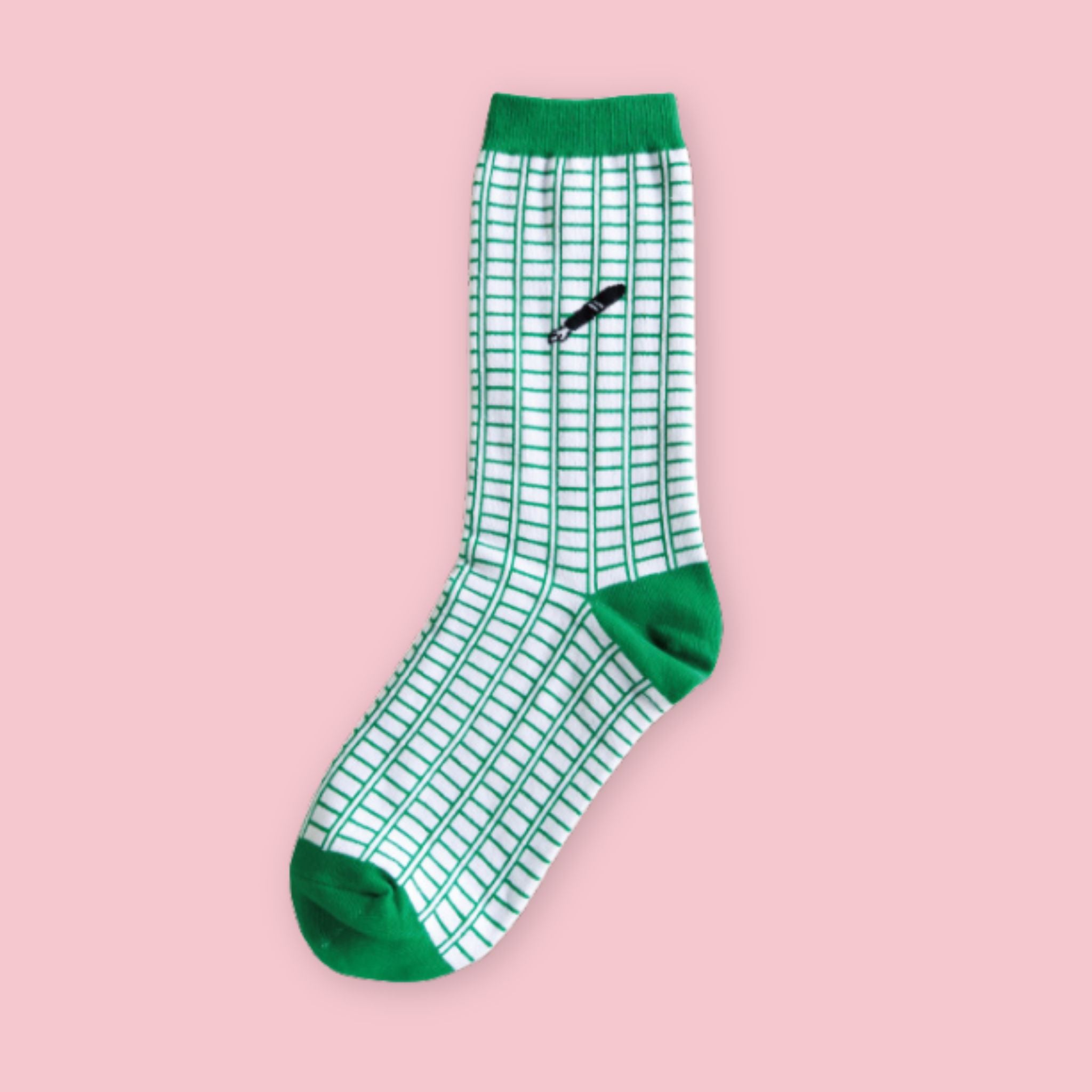 Garapago Socks in Manuscript Paper style featuring green grid pattern with illustrated pen on a crew sock with green cuff and toe on a pink background