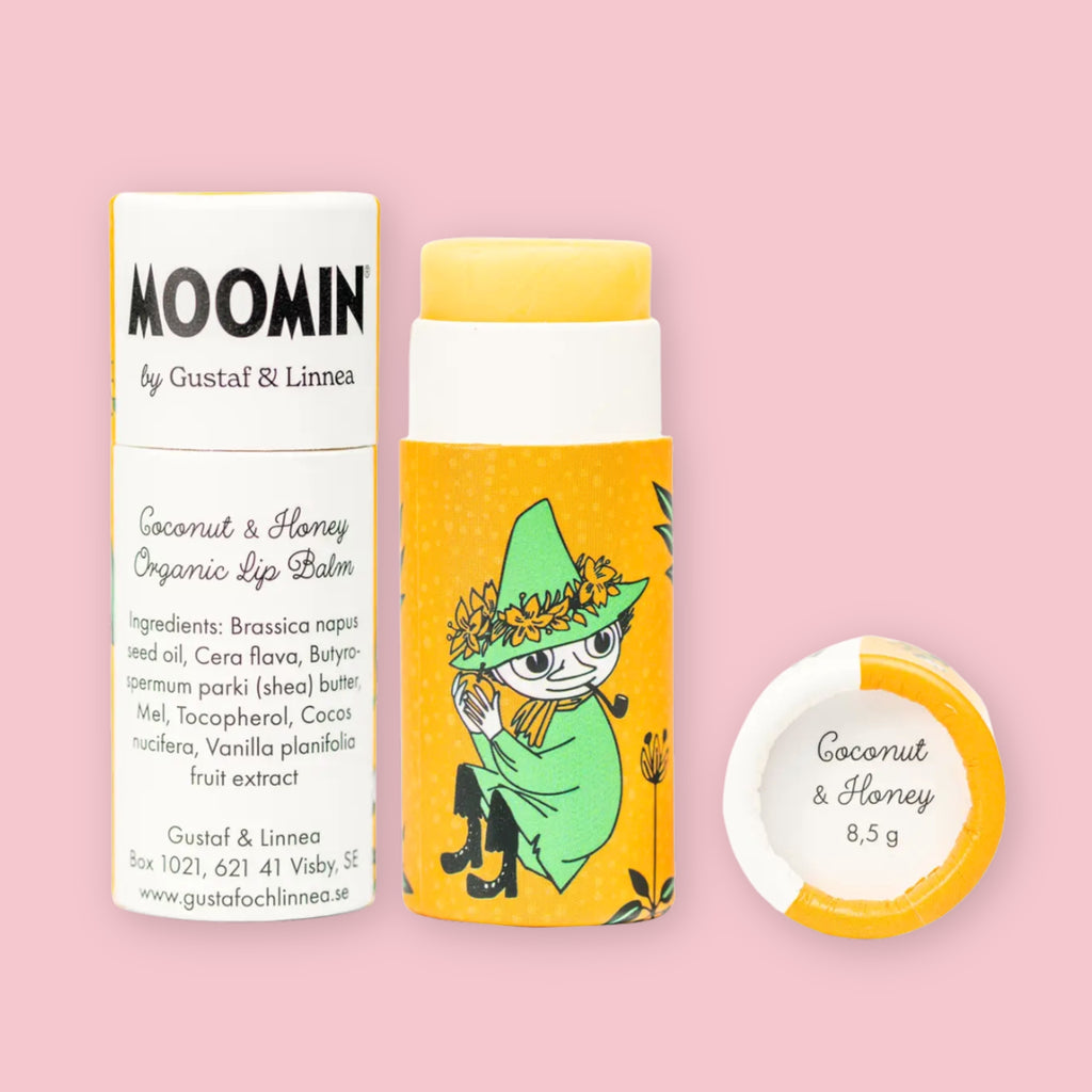 Open Coconut & Honey Moomin lip balm tube with yellow balm visible and ingredients label, illustrated with the Snufkin character on yellow packaging, next to the round lid printed with "Coconut & Honey 8,5 g"