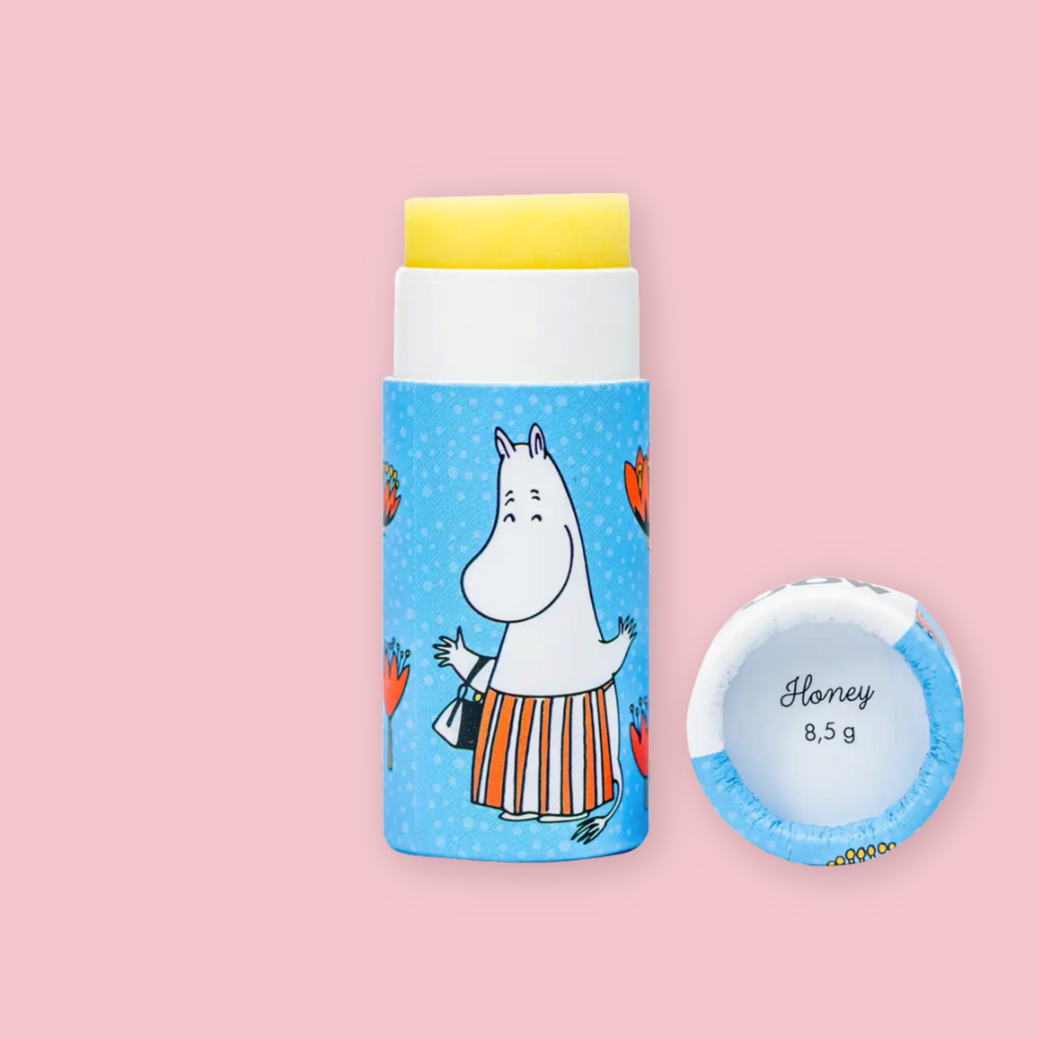 Open Honey Moomin lip balm tube with yellow balm visible, illustrated with Moominmamma on blue packaging, next to the round lid printed with "Honey 8,5 g"