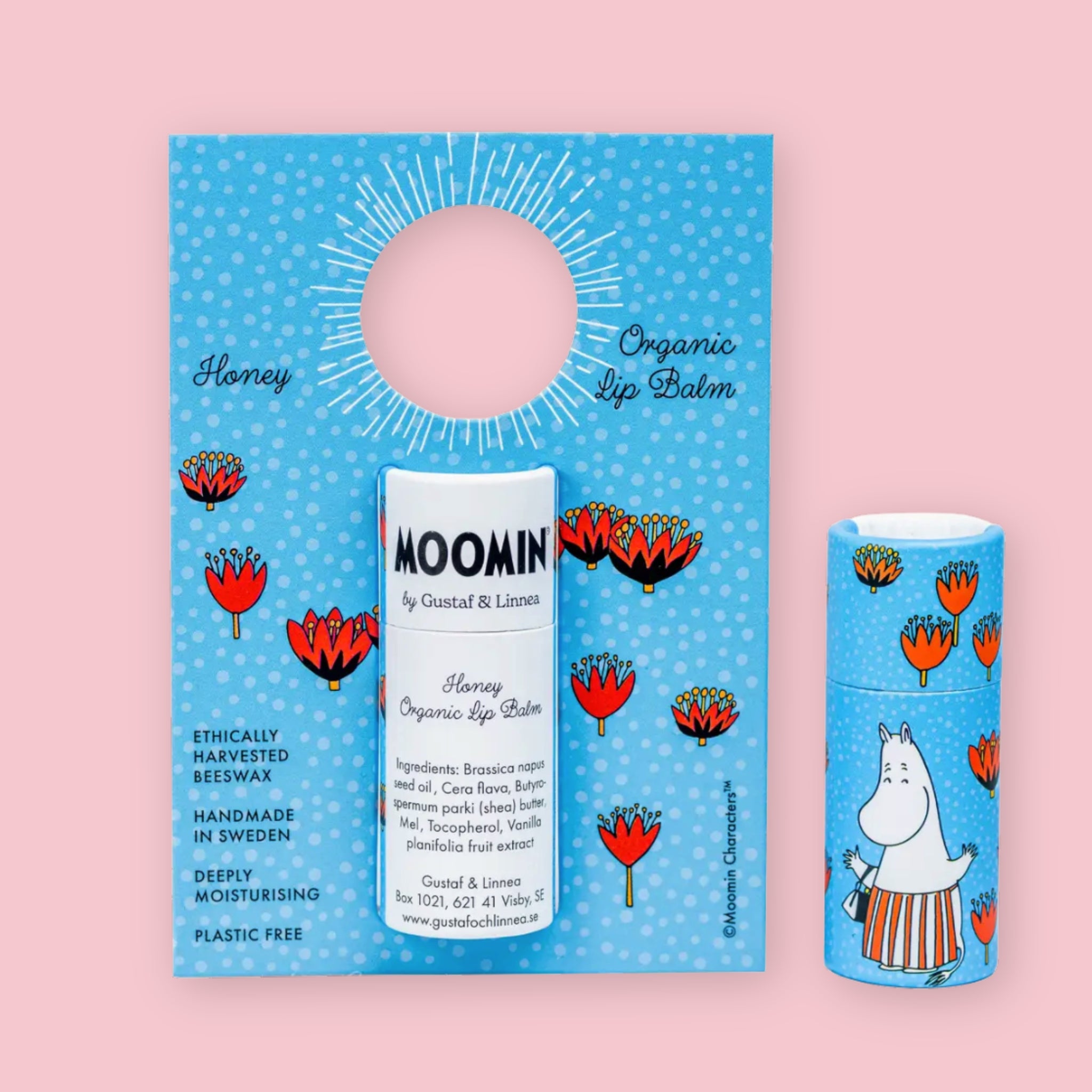 Honey Moomin Organic Lip Balm on its illustrated cardboard display card with floral details, next to a second sealed tube showing the Moominmamma character design, against a pink background