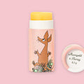 Open Marigold & Honey Moomin lip balm tube with yellow balm visible, illustrated with the Sniff character on pink packaging, next to the round lid printed with "Marigold & Honey 8,5 g"