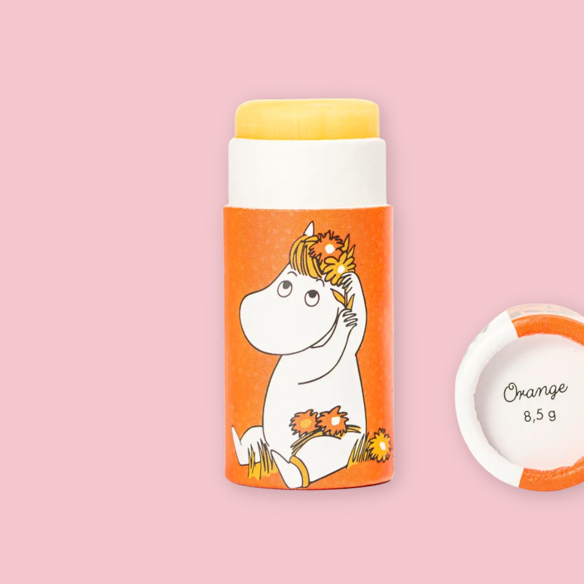 Open Orange Moomin lip balm tube with yellow balm visible, illustrated with Snorkmaiden holding flowers on orange packaging, next to the round lid printed with "Orange 8,5 g"