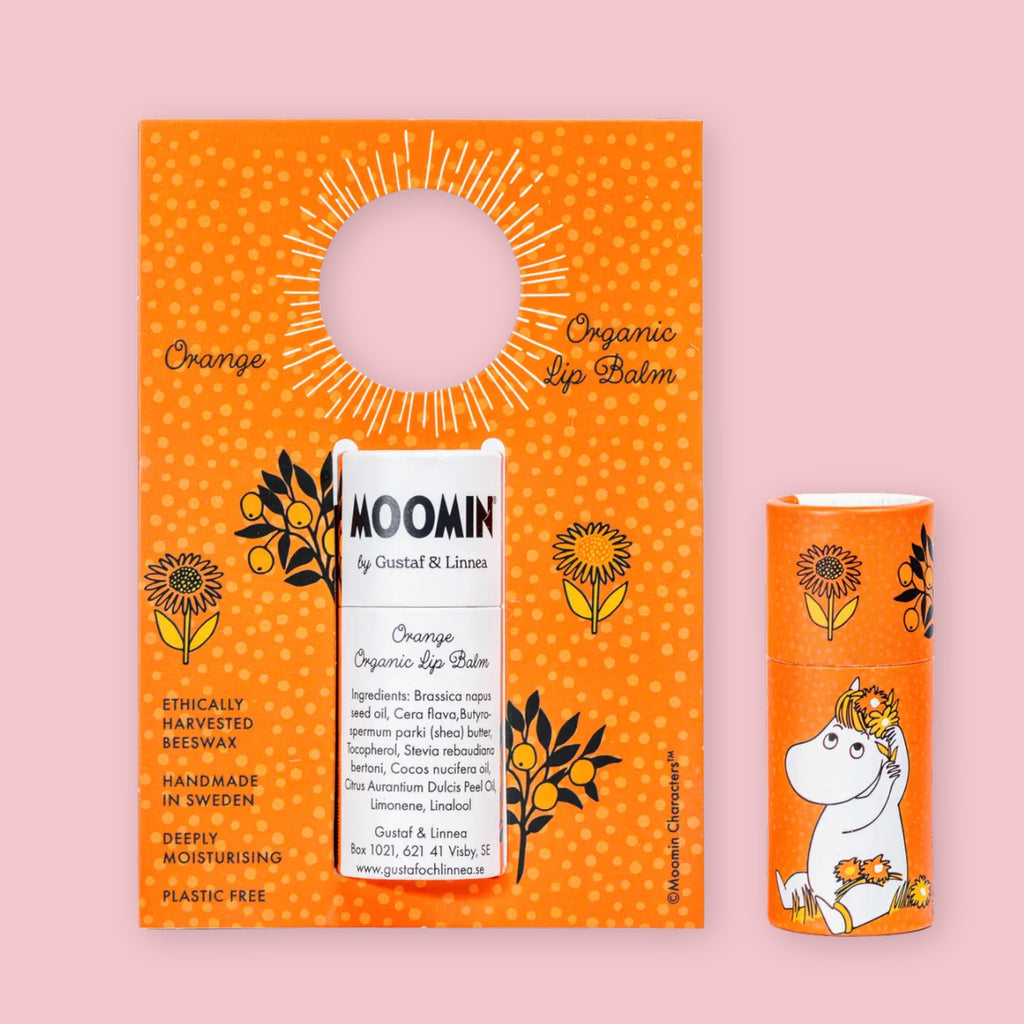 Orange Moomin Organic Lip Balm on its illustrated cardboard display card with floral details, next to a second sealed tube showing the Snorkmaiden character design, against a pink background