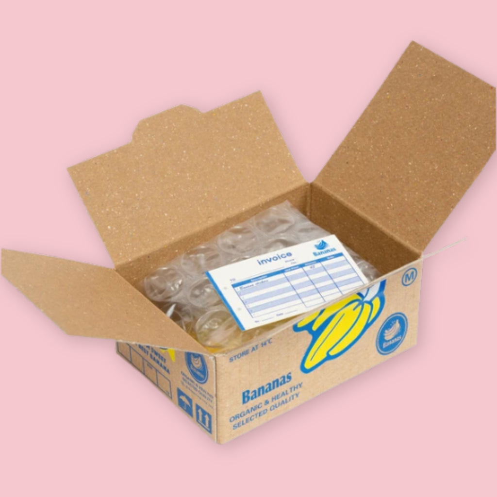 Open Hako sticker box showing bubble-wrapped stickers and a blue invoice inside, with the kraft brown Bananas crate packaging visible on the exterior, on a pink background.