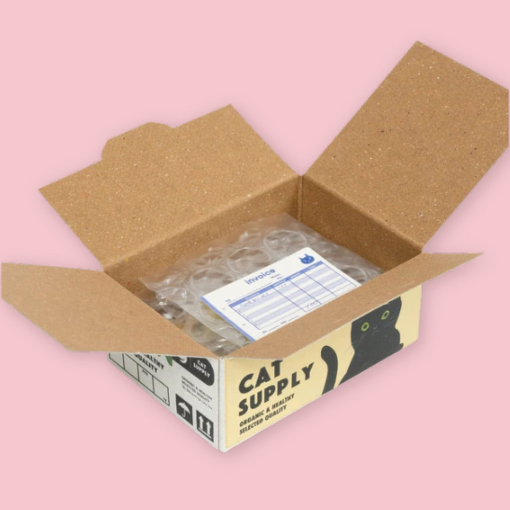 Open Hako sticker box showing bubble-wrapped stickers and a blue invoice inside, with the cream and black Cat Supply packaging visible on the exterior, on a pink background.