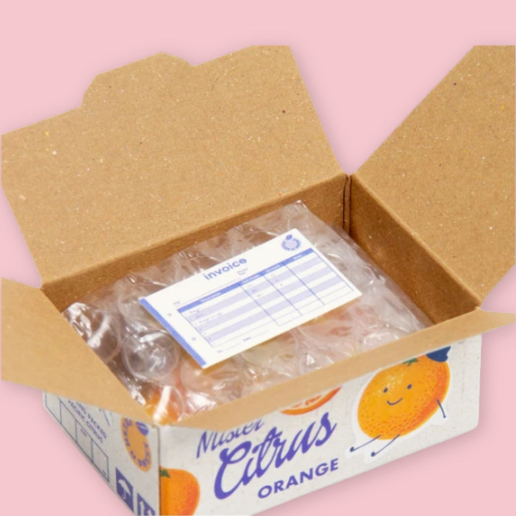 Open Hako sticker box showing bubble-wrapped stickers and an invoice inside, with the white "Mister Citrus Orange" packaging visible on the exterior, on a pink background.