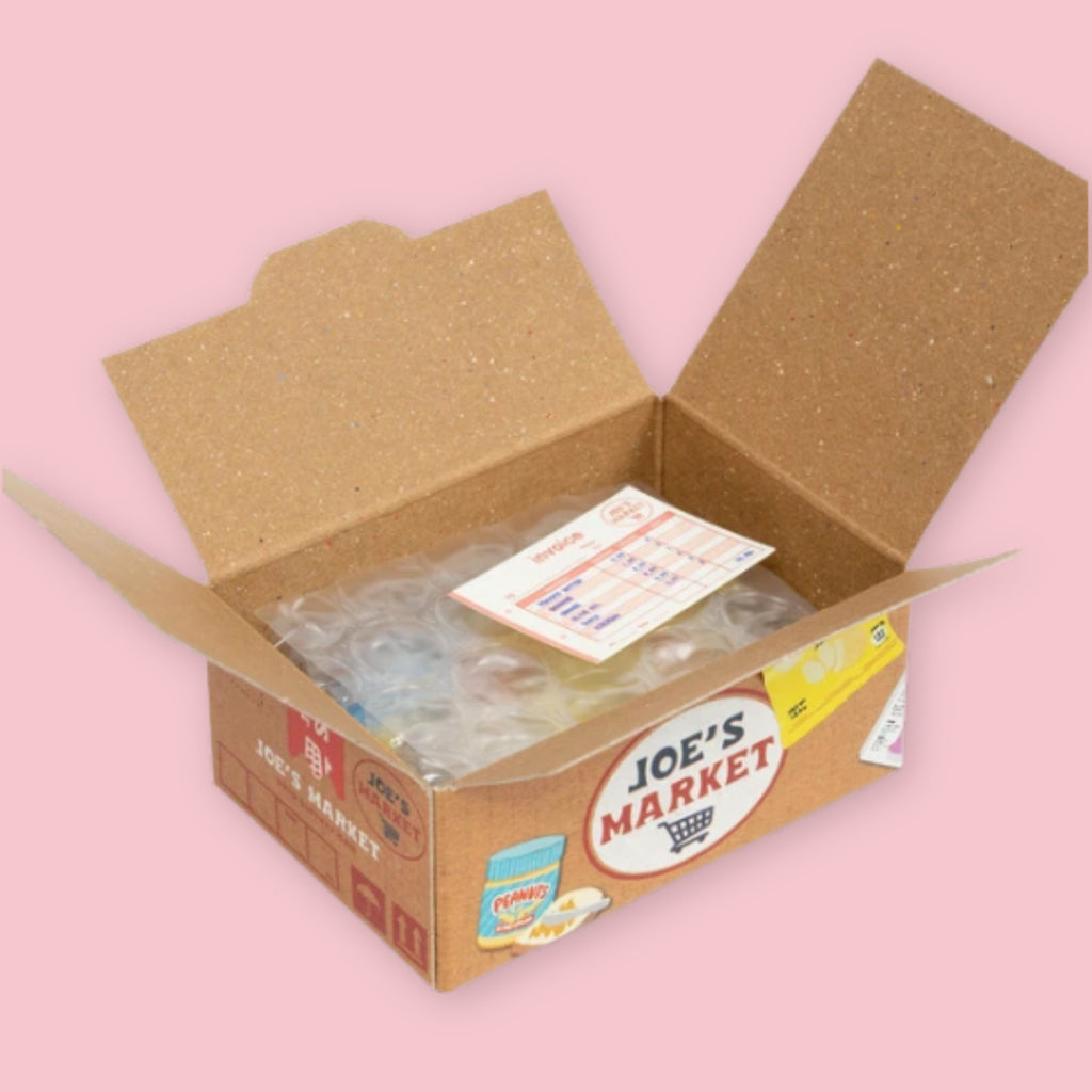 Open Hako sticker box showing bubble-wrapped stickers and a receipt-style invoice inside, with the kraft brown Joe's Market packaging visible on the exterior, on a pink background.