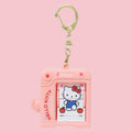 Pink plastic camera shaped keychain with a gold swivel clasp, showing Hello Kitty in blue overalls surrounded by hearts and apples on the flip book pages visible through the front window, against a solid pink background.