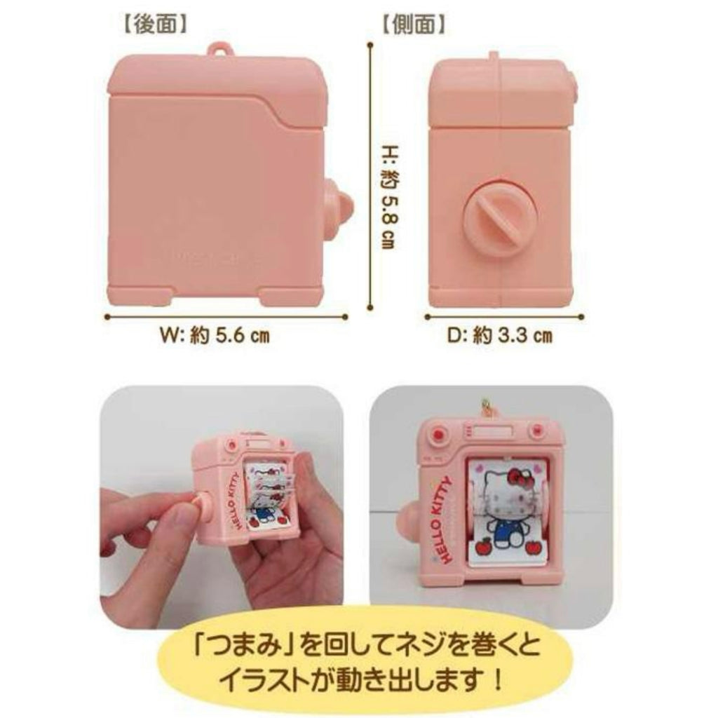 Diagram showing the back and side views of the pink camera shaped keychain with dimensions labeled in Japanese, along with two photos of hands turning the side crank to flip through the Hello Kitty illustrations, captioned with Japanese text explaining how to wind the knob.