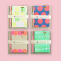 Four Iro Iro Neon Memo Pads with assorted patterned loose sheets held together by gold binder clips on a pink background