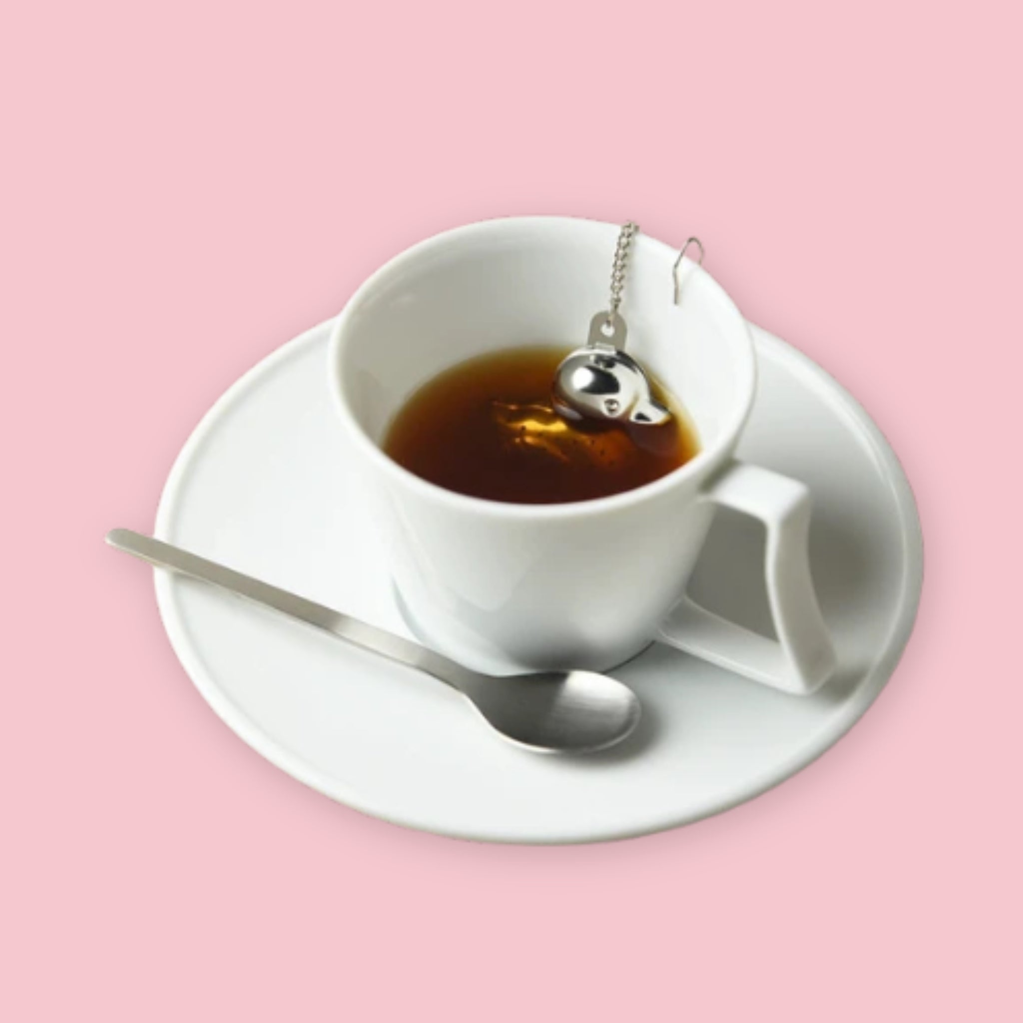 Duck tea strainer steeping in a white teacup and saucer on a pink background