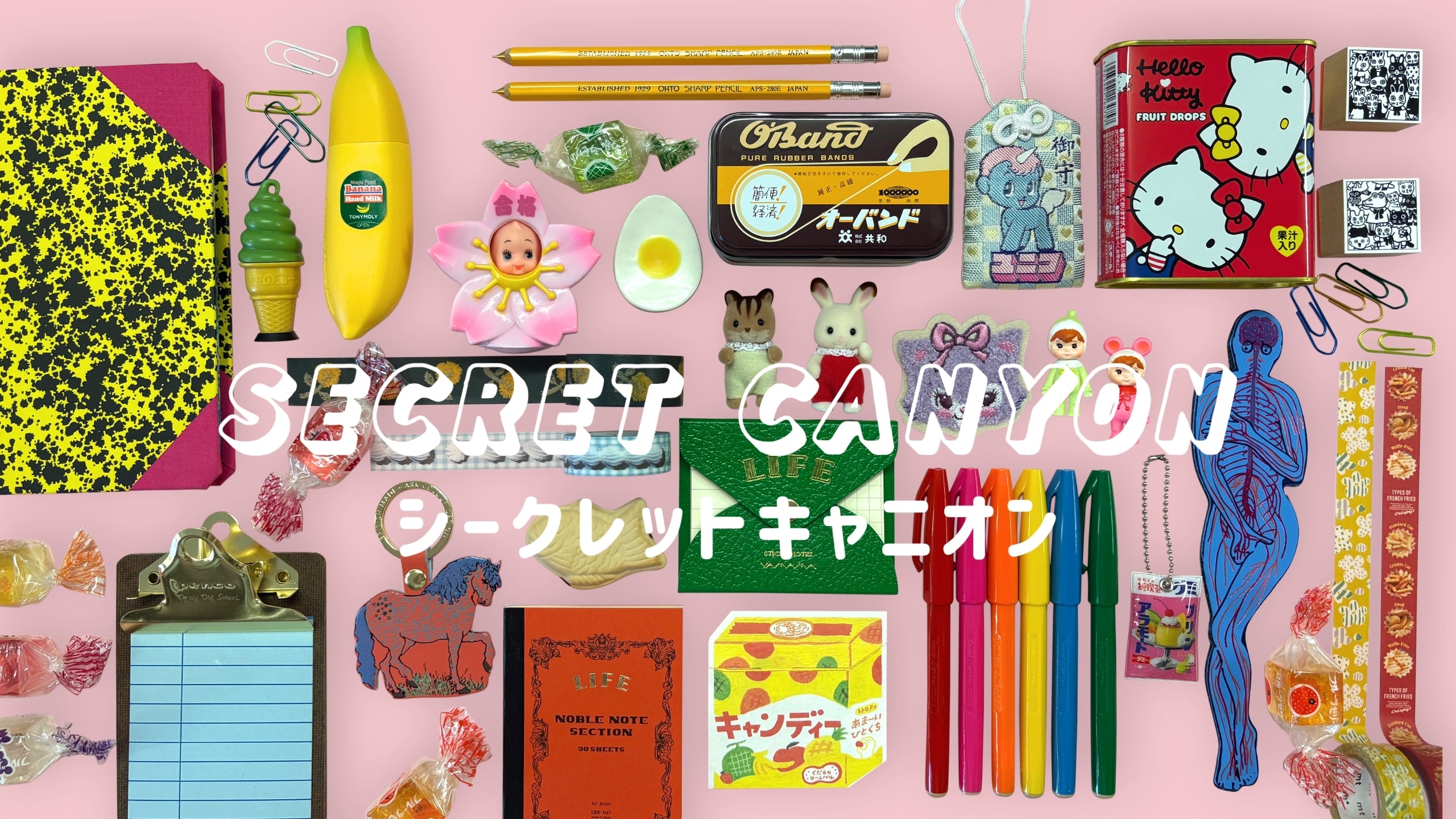 Collage of Secret Canyon stationery and gift items on a pastel pink background, including notebooks, pencils, washi tape, candy, clips, pens, charms, mini figures, Hello Kitty tin, and Japanese text reading “シークレットキャニオン.”