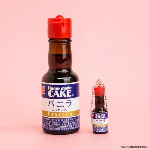 Bottle of Home Made Cake vanilla essence with a miniature keychain version next to it on a pink background
