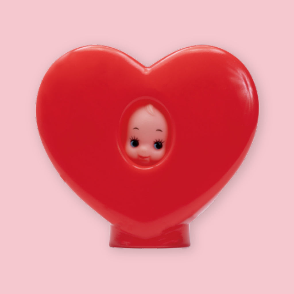 Red heart-shaped Obitsu Kewpie hood doll with Kewpie face peeking through the center, shown on a pink background.