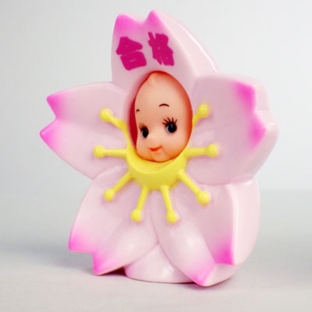 Side view of Obitsu Kewpie doll dressed as a cherry blossom, with pink petals and Japanese characters on the top petal.