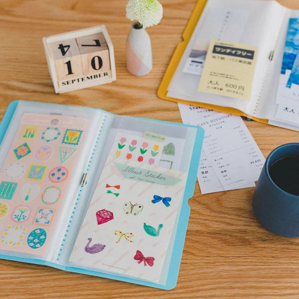 Open sticker album with colorful stickers on a wooden desk with a cup and calendar.