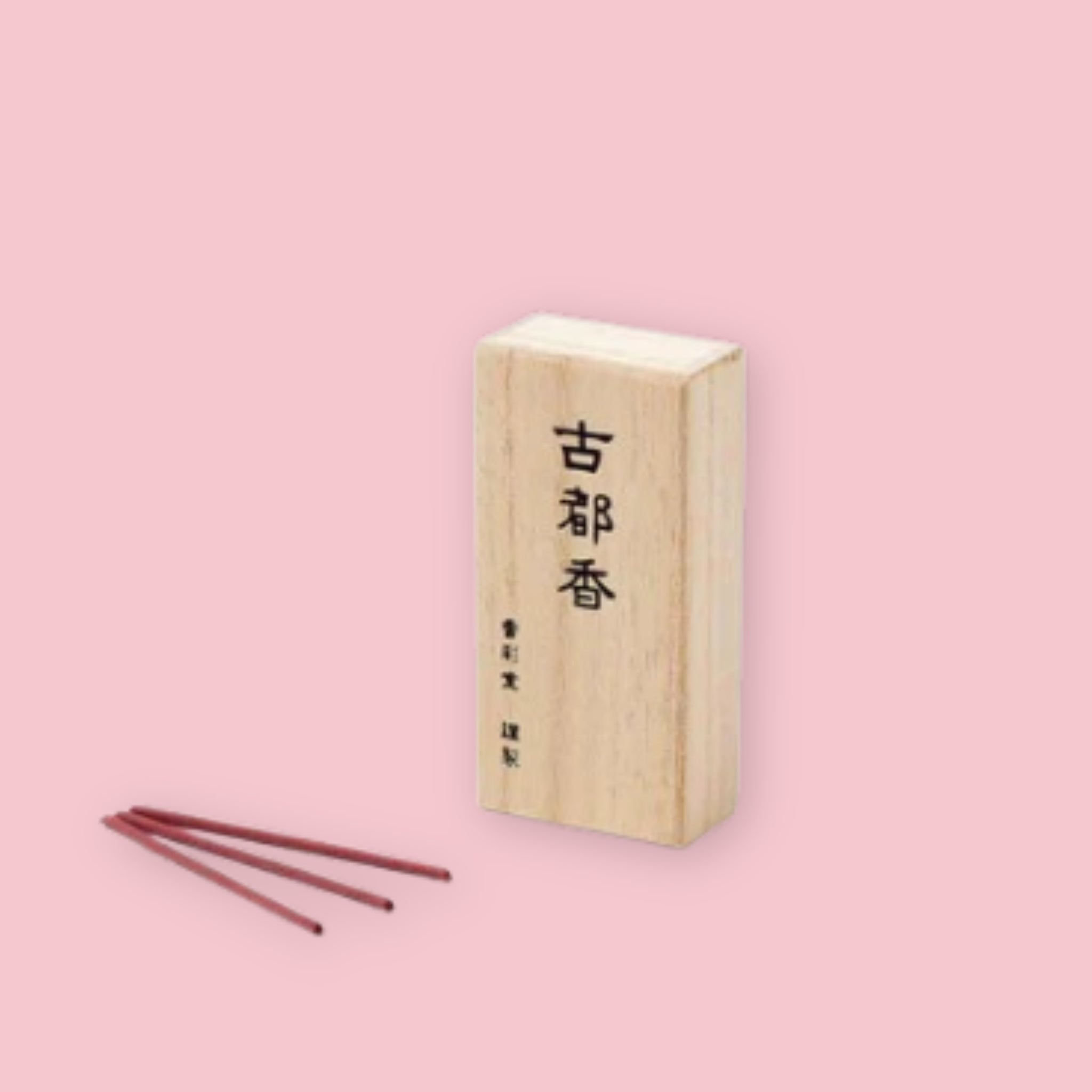 Kousaido Ancient Capital incense box with kanji lettering, shown beside three loose maroon incense sticks, on a pink background.